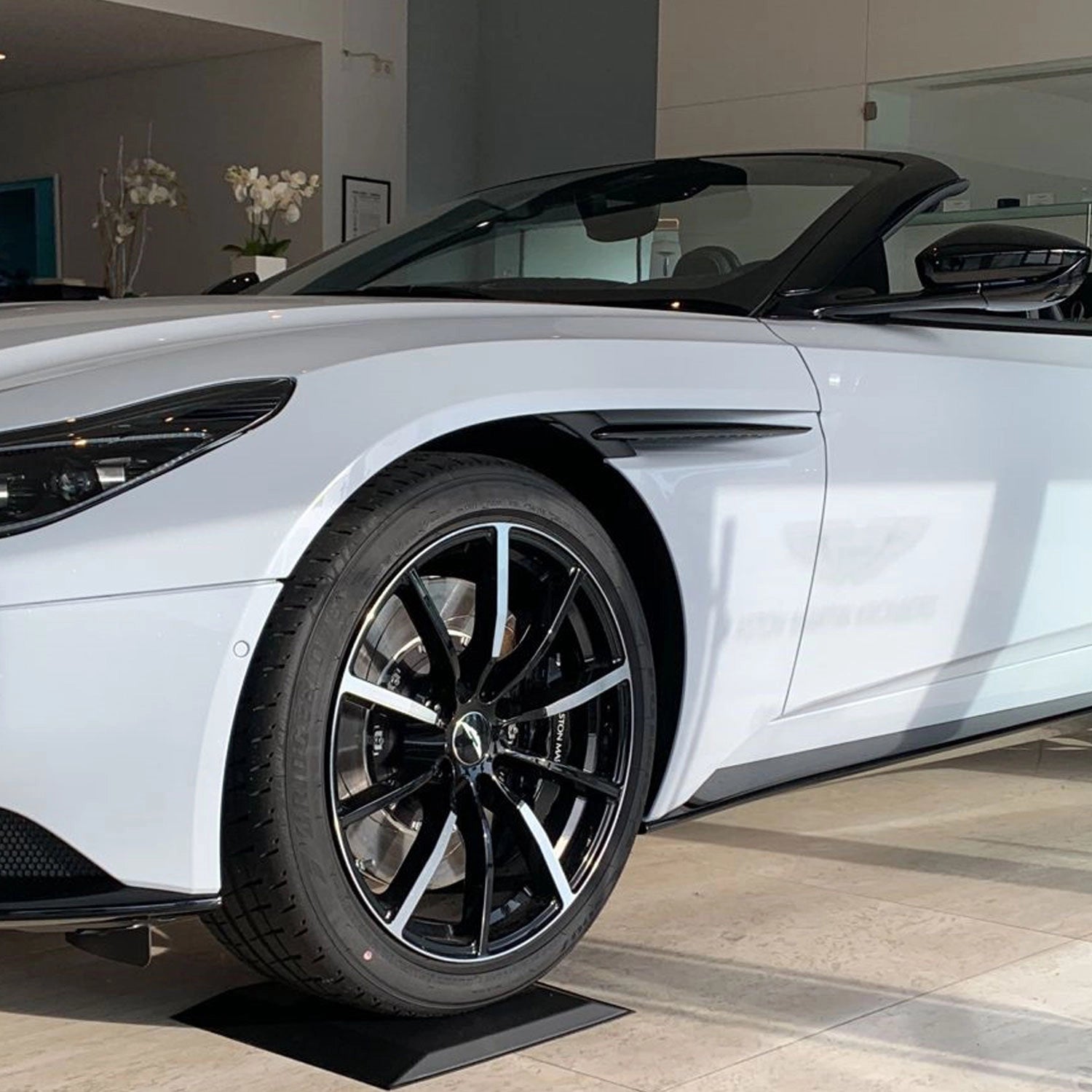 Ein weißer Sportwagen steht in einem Autohaus auf Reifenschuhen aus Flexigel® Tyre Care Reifenschonern.